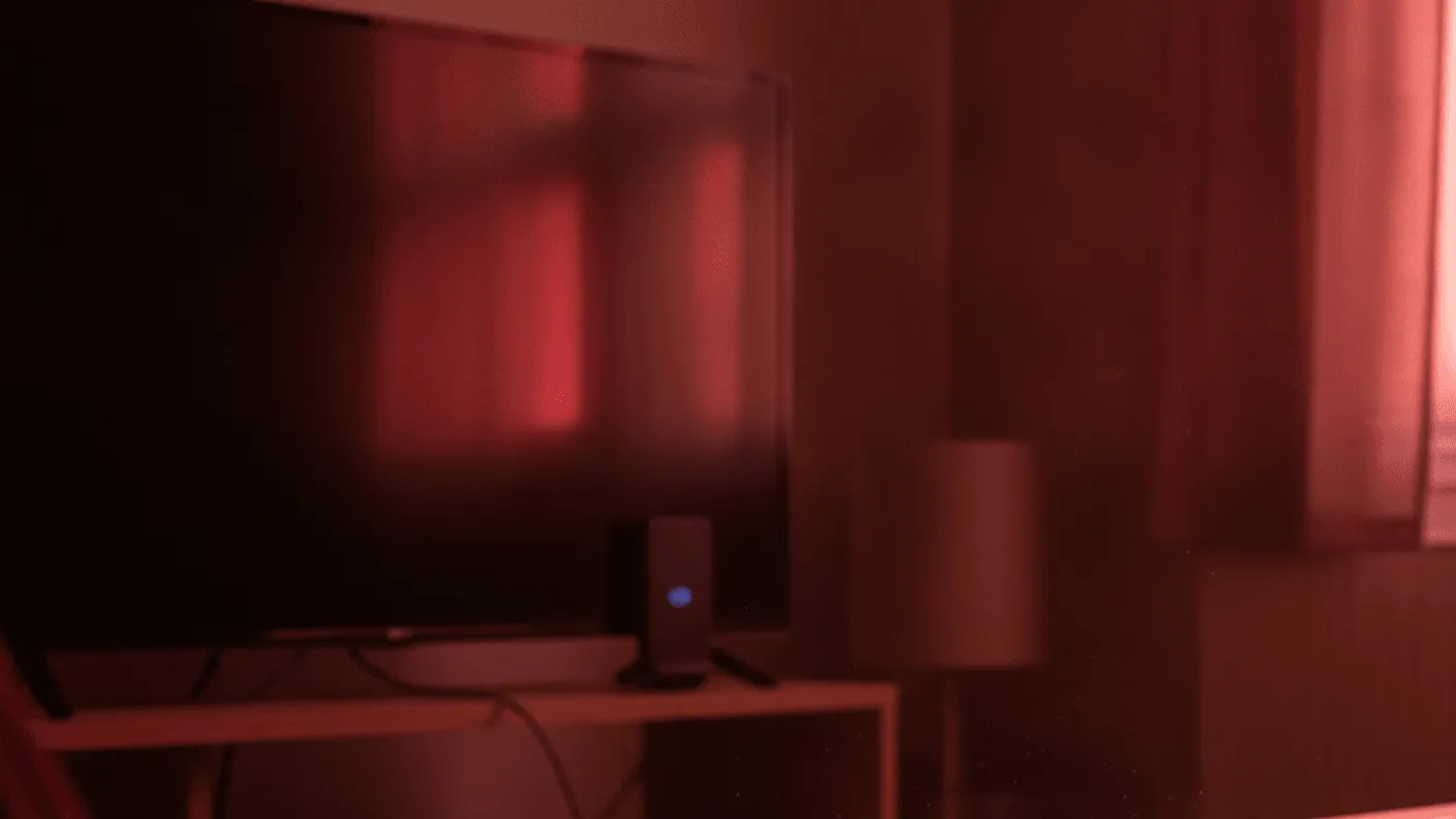 A television, a media player, and a remote control sit in a dimly lit room with a red cast.