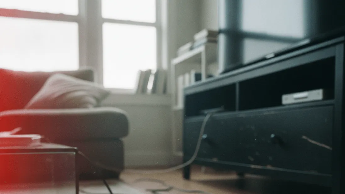A hand holds a smartphone showing a blank clock timer app beside a television remote on a rug, midday light from a window.
