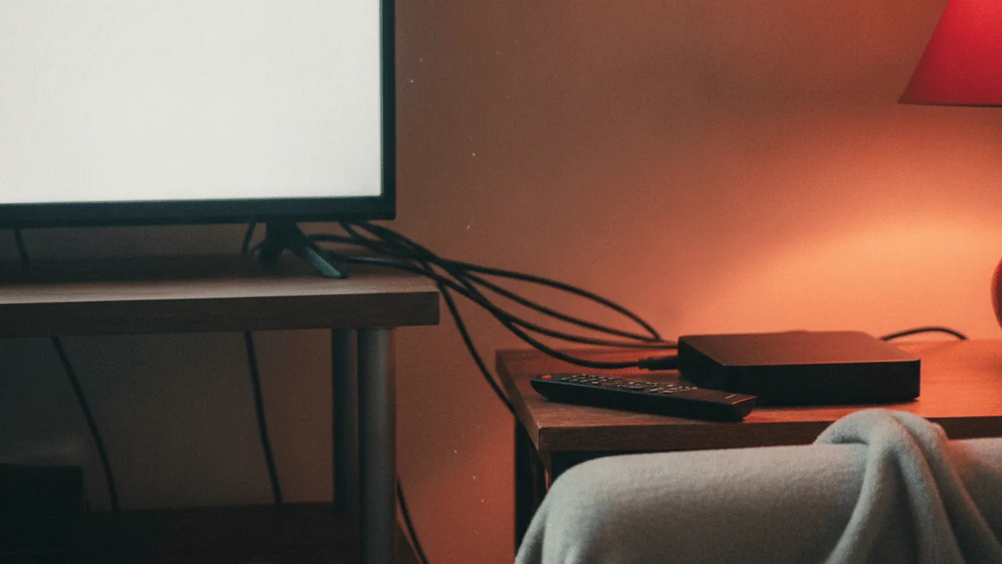 A person holding a mug watches a television with a streaming box nearby.