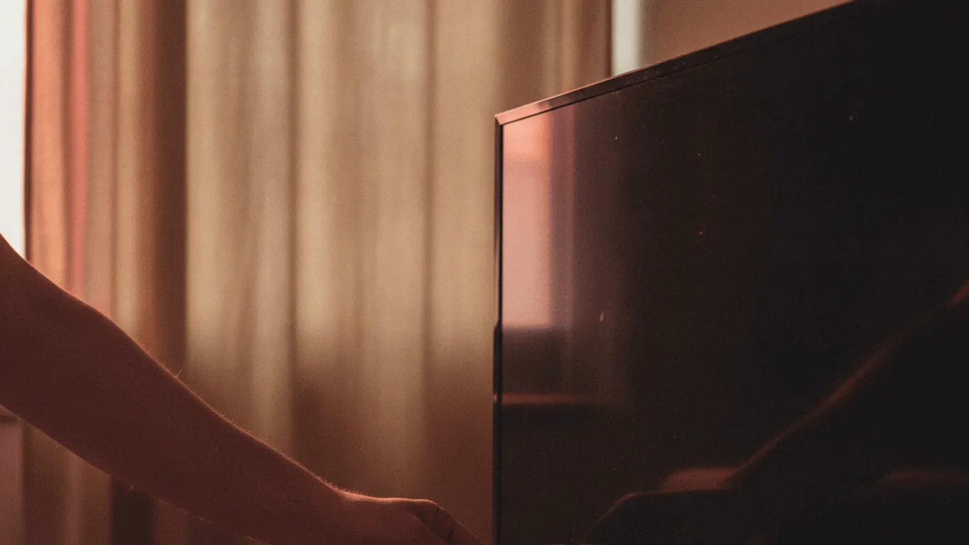 A hand pushes a 4K streaming stick into the back of a television in a dim living room.